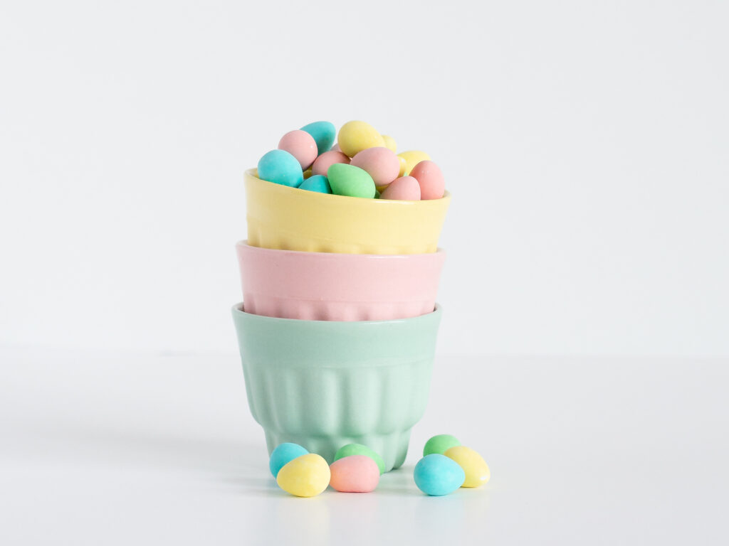 A stack of three small cups in yellow, pink, and green with tiny chocolate eggs